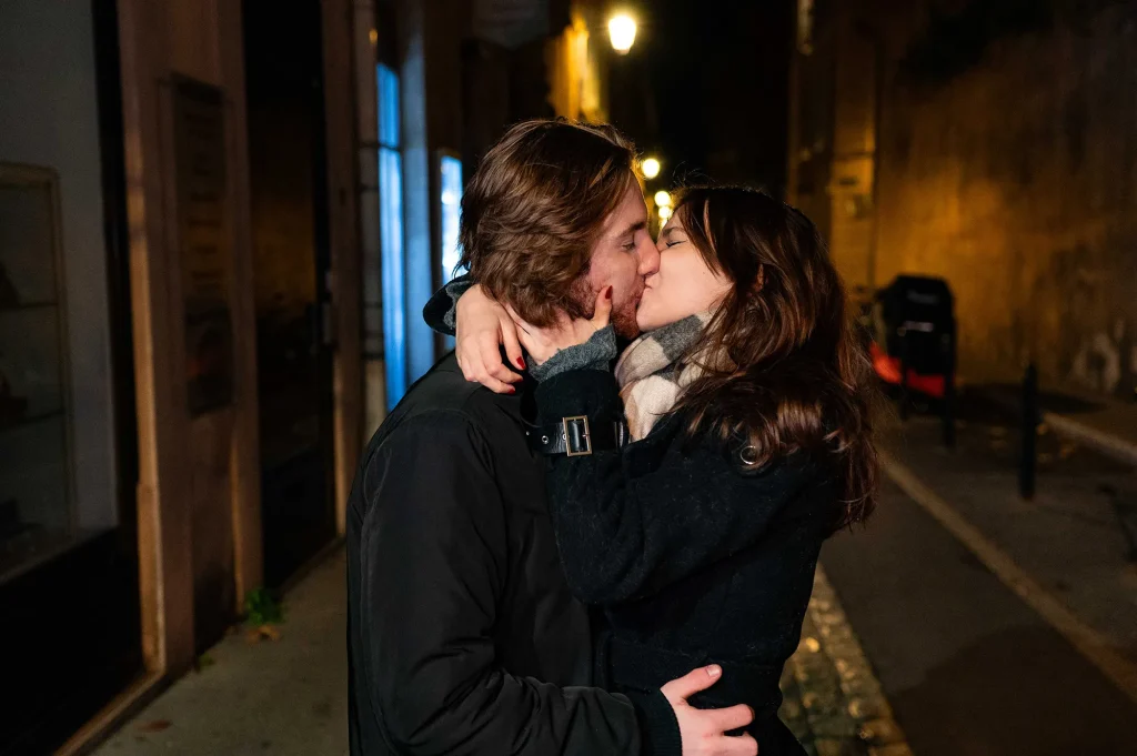 Couple tenderly kissing in a quiet alley of Aix-en-Provence city centre, at night in winter, under warm lighting