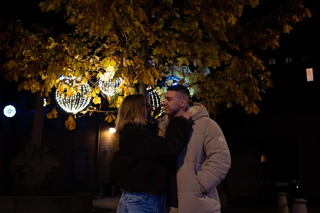 Couple during a nighttime photoshoot in winter in Aix-en-Provence, under tree illuminations and glowing lanterns