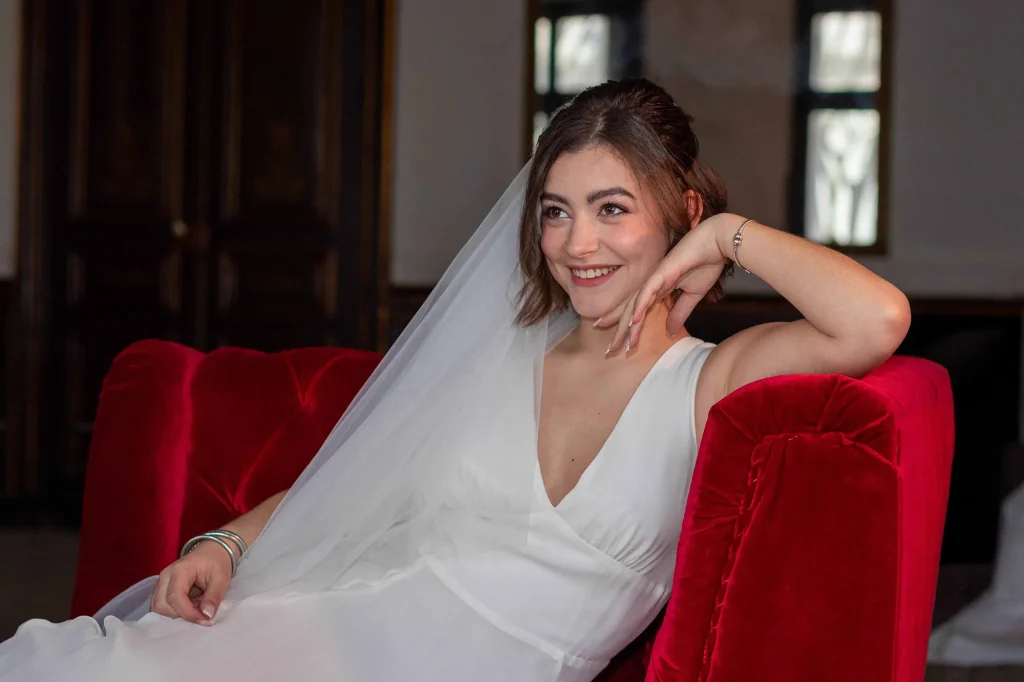 Bride wearing a veil, seated on a red velvet armchair in a historic house in Nîmes, South of France.