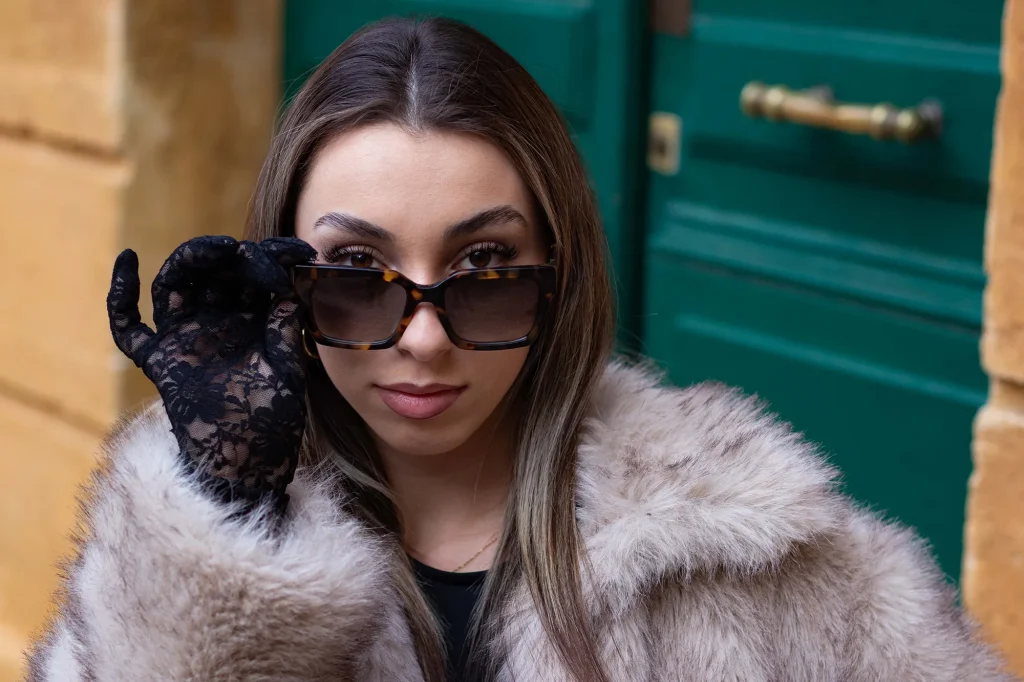 Close-up portrait of a woman wearing sunglasses and black gloves in an urban setting in Aix-en-Provence