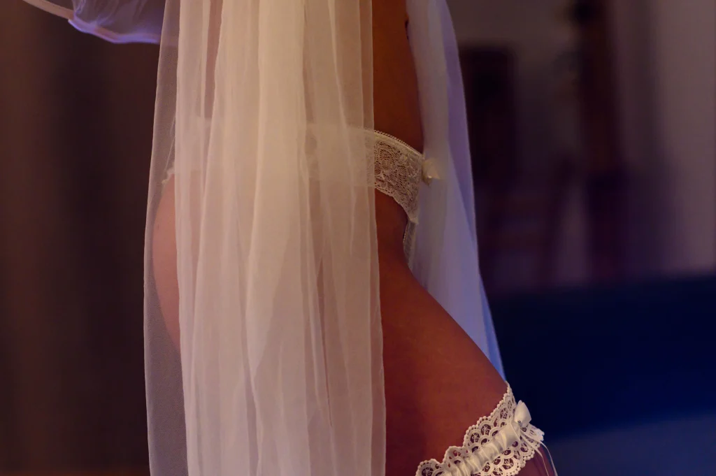 Profil de future mariée sous un voile blanc avec lingerie et jarretière pendant une séance bridal boudoir