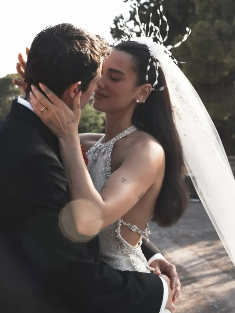 Dua Lipa and Callum Turner in a spontaneous, emotional moment during their outdoor wedding, with a backless dress and tailored suit