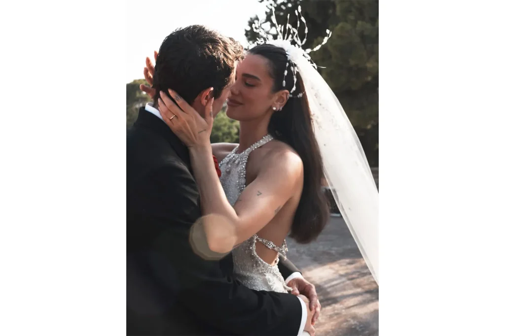Dua Lipa and Callum Turner in a spontaneous, emotional moment during their outdoor wedding, with a backless dress and tailored suit