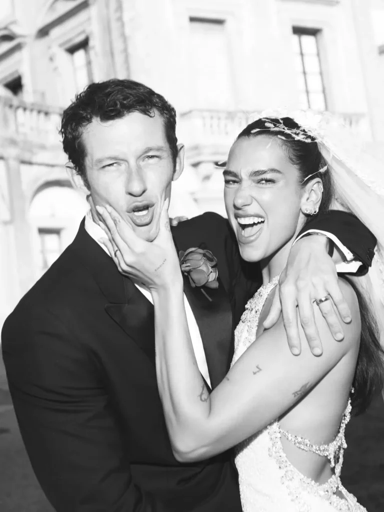 Dua Lipa et Callum Turner en train de rire lors de leur mariage à Palerme, robe de mariée à dos nu et costume noir élégant