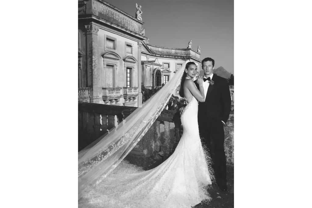 Dua Lipa et Callum Turner en robe de mariée à traîne devant un bâtiment historique lors de leur mariage en extérieur à Palerme