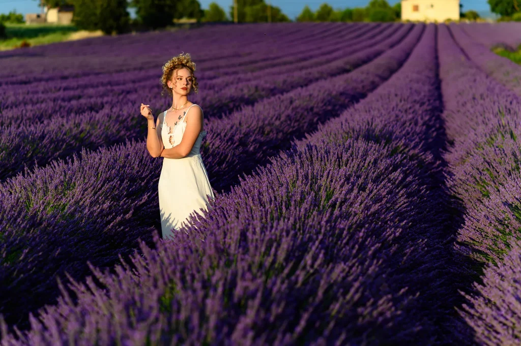 Bride in a long white dress standing in the middle of a lavender field in Puy-Sainte-Réparade, arms crossed, sophisticated hairstyle, immersive purple ocean atmosphere