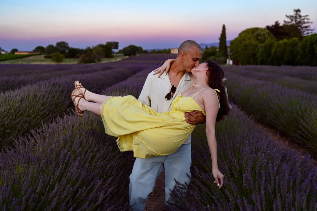 Couple s’embrassant dans un champ de lavande en Provence, l’homme portant une chemise blanche et la femme une robe jaune longue, ambiance romantique au coucher de soleil