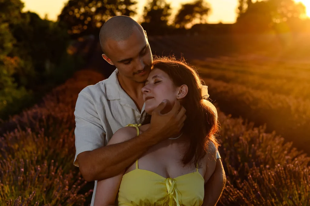 Couple s’étreignant tendrement dans un champ de lavande au coucher du soleil, l’homme en chemise claire et la femme en robe jaune, ambiance romantique et lumière dorée pour immortaliser leur amour en Provence