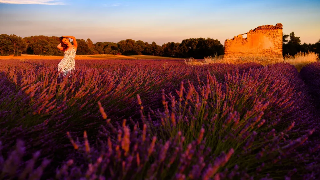 Woman in a floral dress standing in a lavender field at sunset in Provence, with a stone ruin in the background, golden-red light