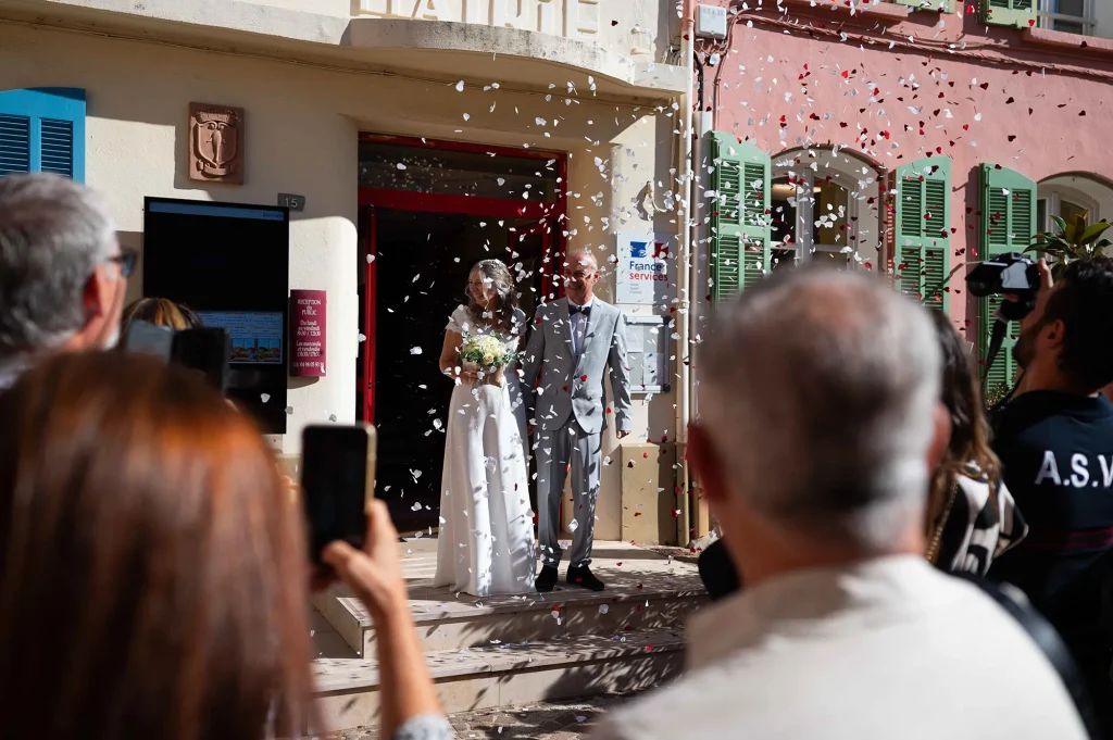 Newlyweds smiling under a shower of confetti outside the town hall in Rougiers