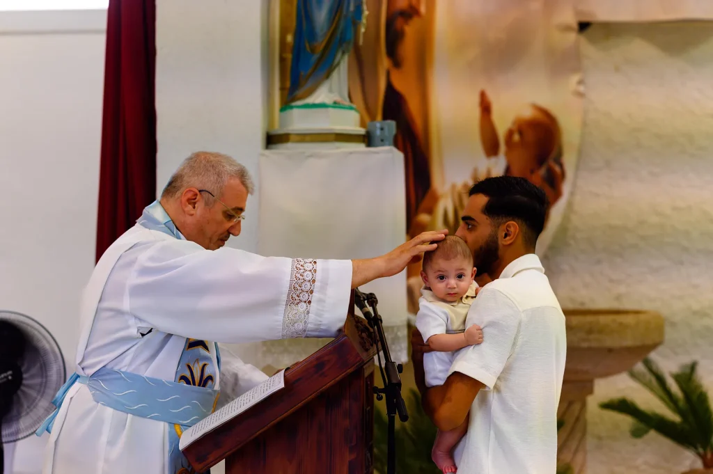 The priest places his hand on the baby's head, a family moment captured in Marseille