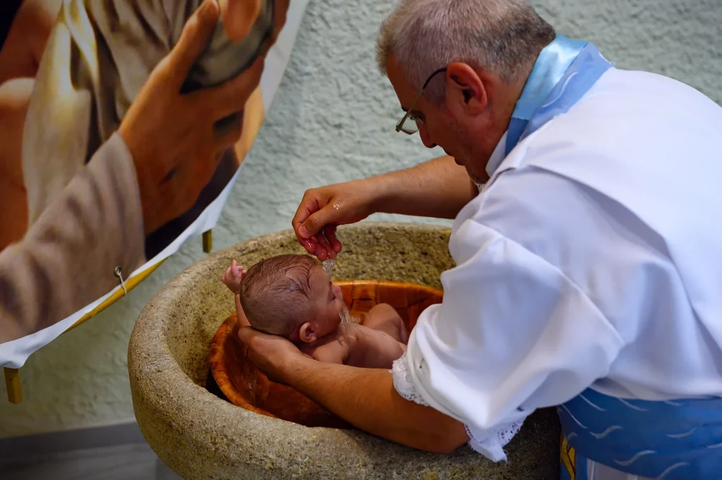 The priest pours water over the baby's head above the stone baptismal font